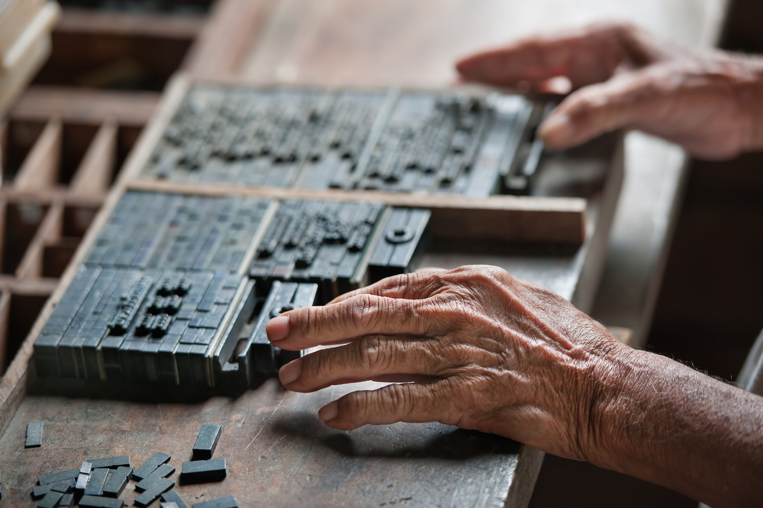 Hände, die scheinbar zu einer betagten Person gehören, sortieren einen Handsatzkasten aus Blei.