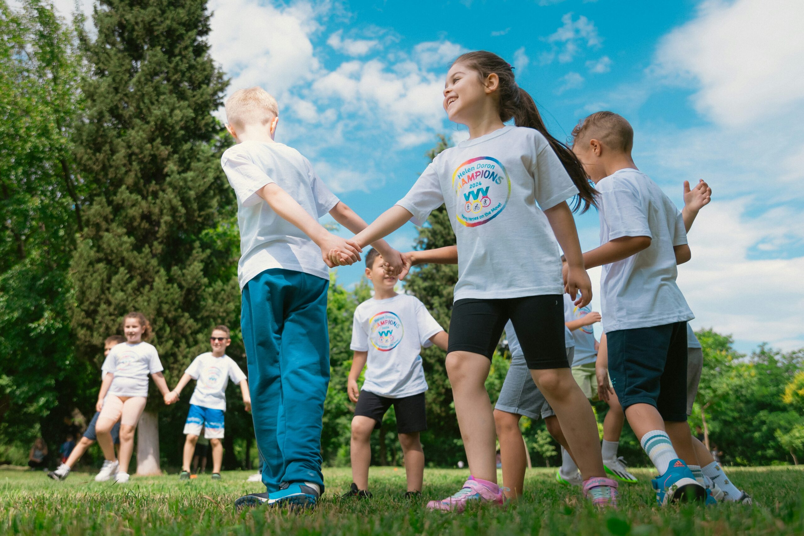 eine Gruppe Kinder, die im Park lachend ein Spiel spielen, bei dem sich an den Händen gehalten werden muss.