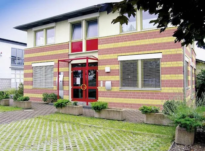 Frontansicht des Firmengebäudes mit Parkplatz und Eingangstür